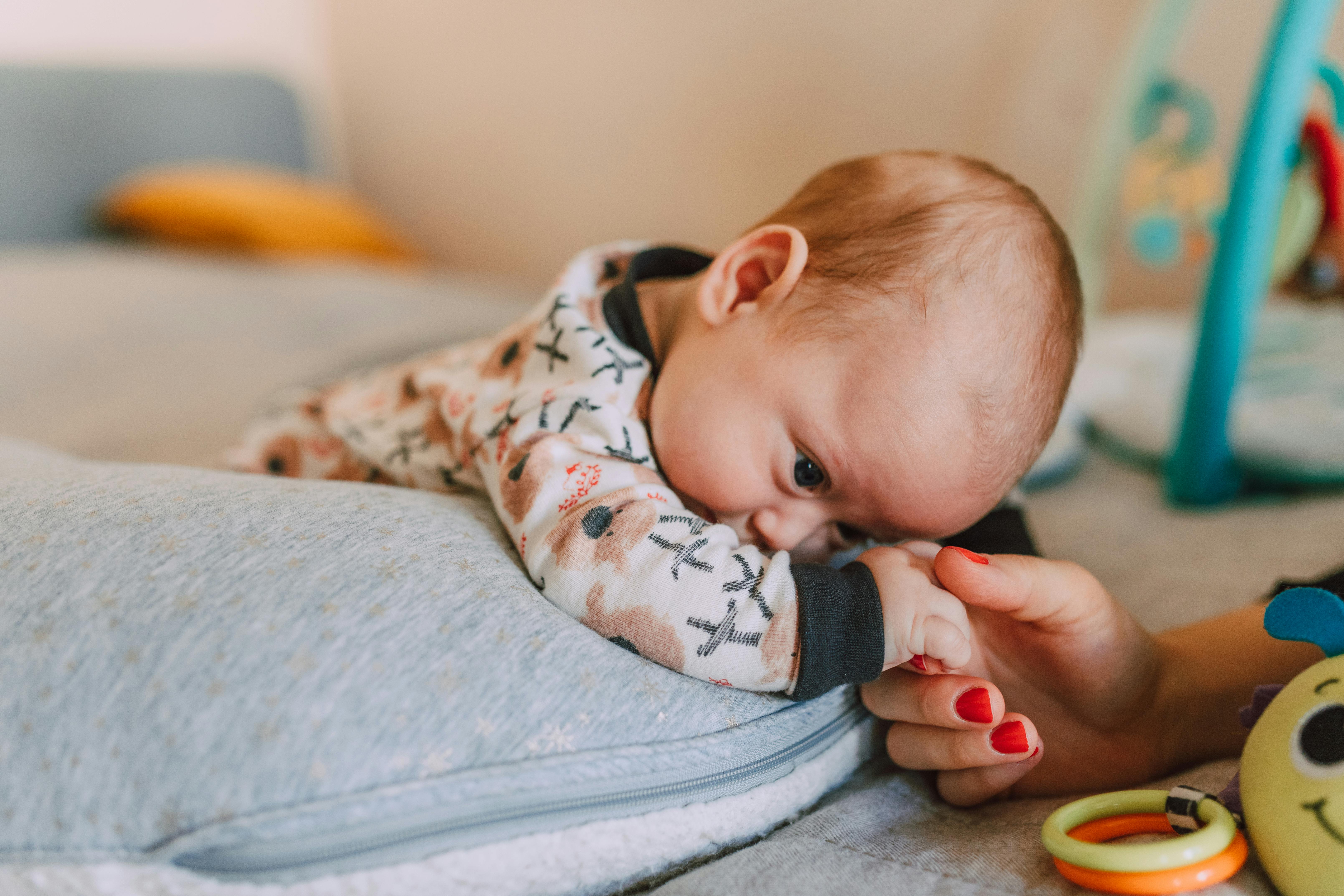 a person holding the hand on a baby lying on a pillow