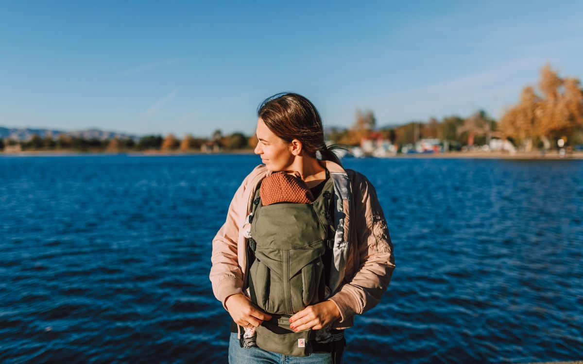 A mother with her baby in a carrier enjoys a sunny day by the water.