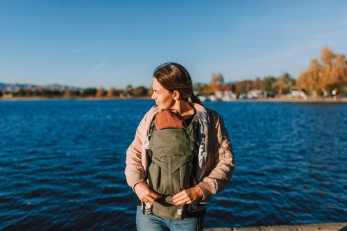 Free A mother with her baby in a carrier enjoys a sunny day by the water. Stock Photo