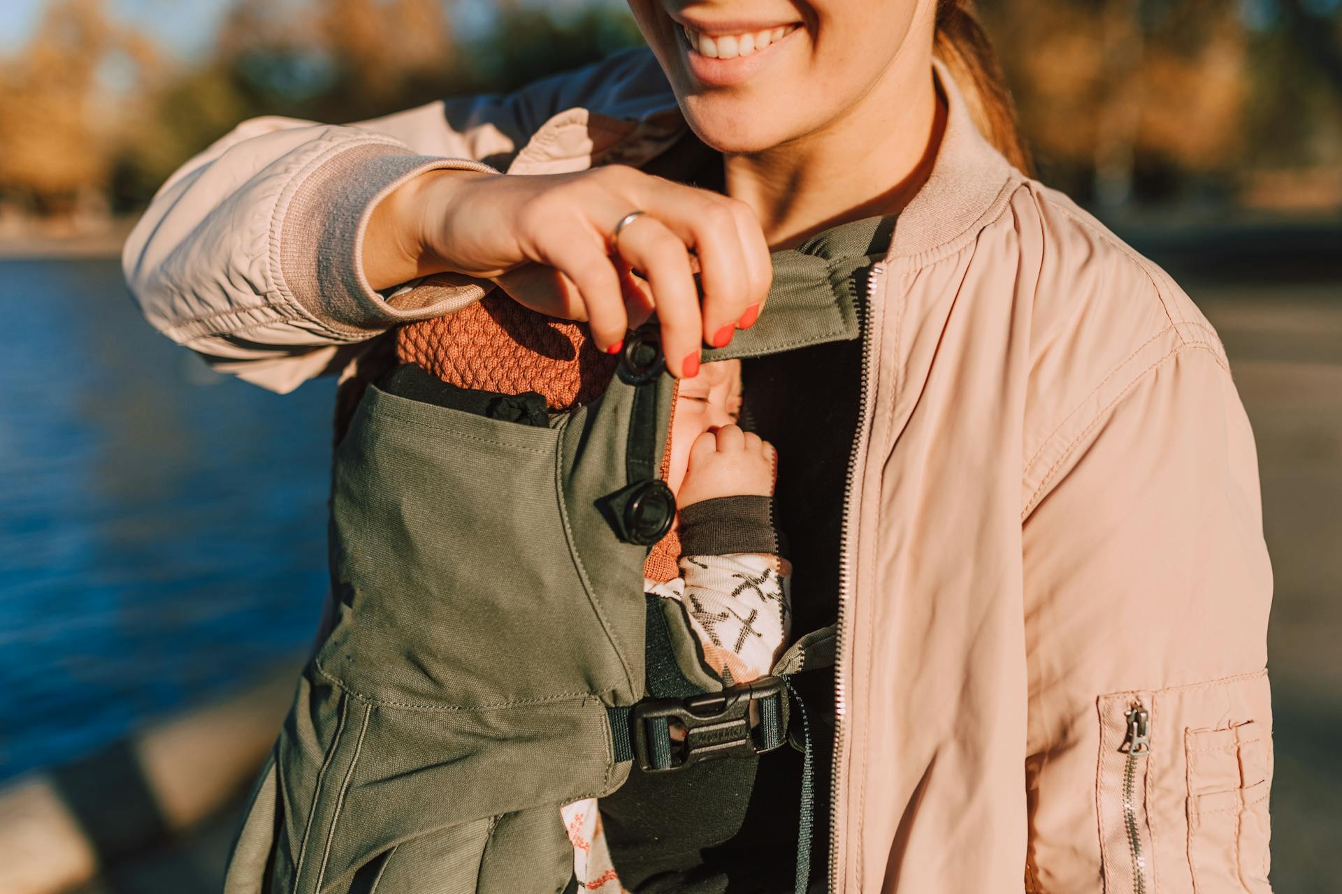 A joyful mother holds her baby in a carrier while enjoying a sunny day outdoors.