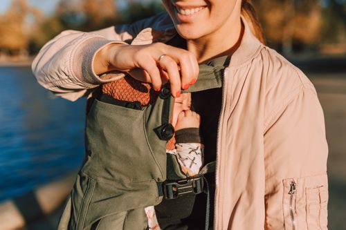 Free A joyful mother holds her baby in a carrier while enjoying a sunny day outdoors. Stock Photo