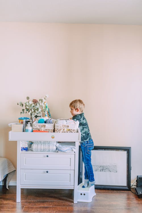 A Boy in Denim Pants Standing Beside the White Drawer