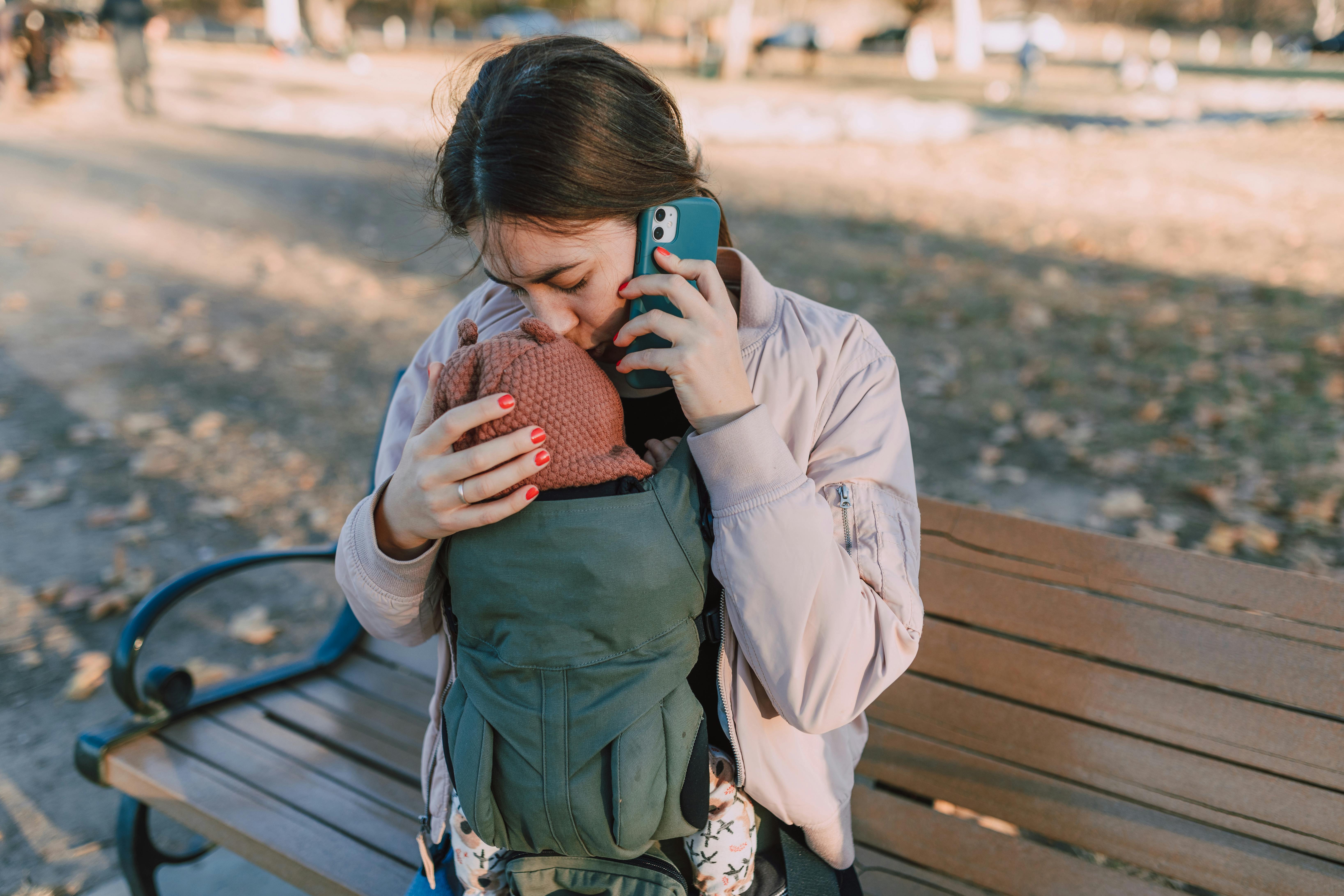 woman sitting on a wooden bench kissing the baby s head