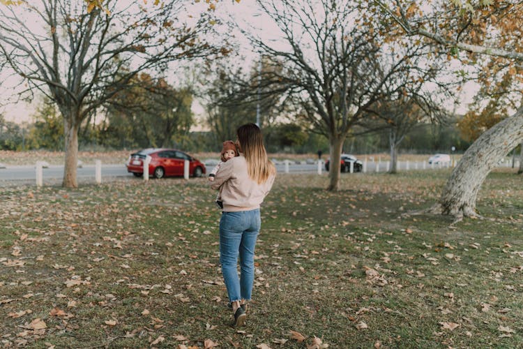 A Woman Walking On Green Grass Carrying A Baby 