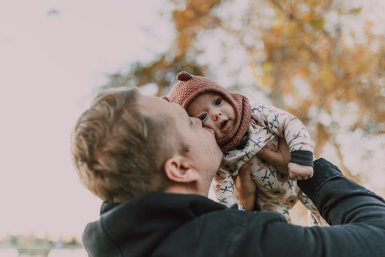 A Man In Black Hoodie Kissing A Baby In Onesie