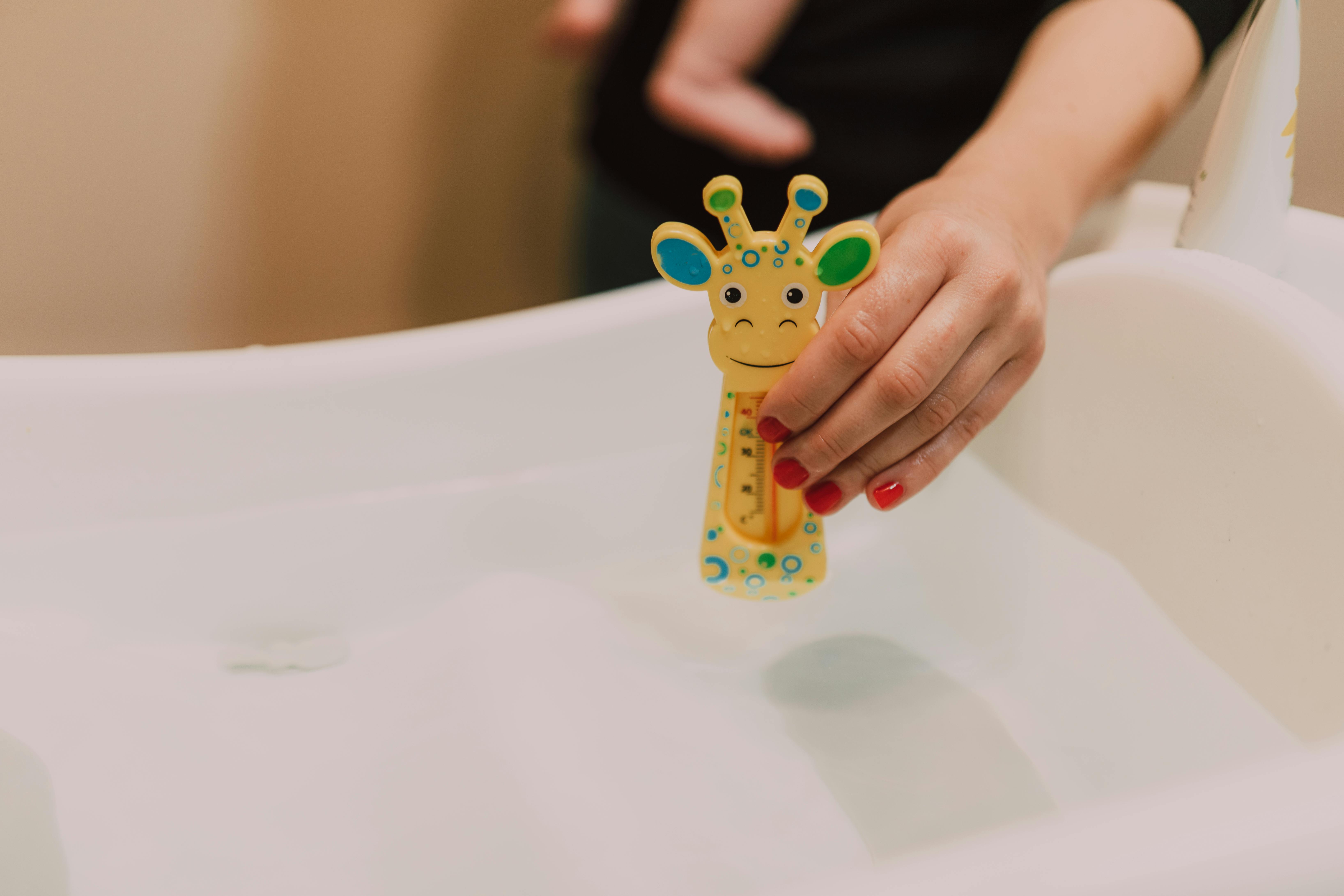 A parent's hand testing the water temperature in a baby tub before placing the baby inside - baby bath essentials