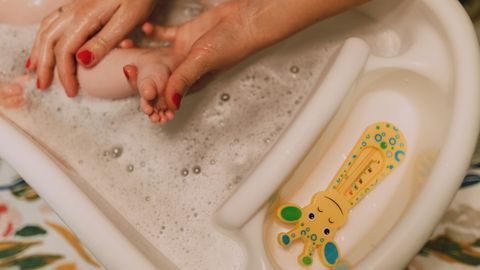 A caring parent gently bathes a baby in a bubbly bathroom scene, showcasing love and hygiene.