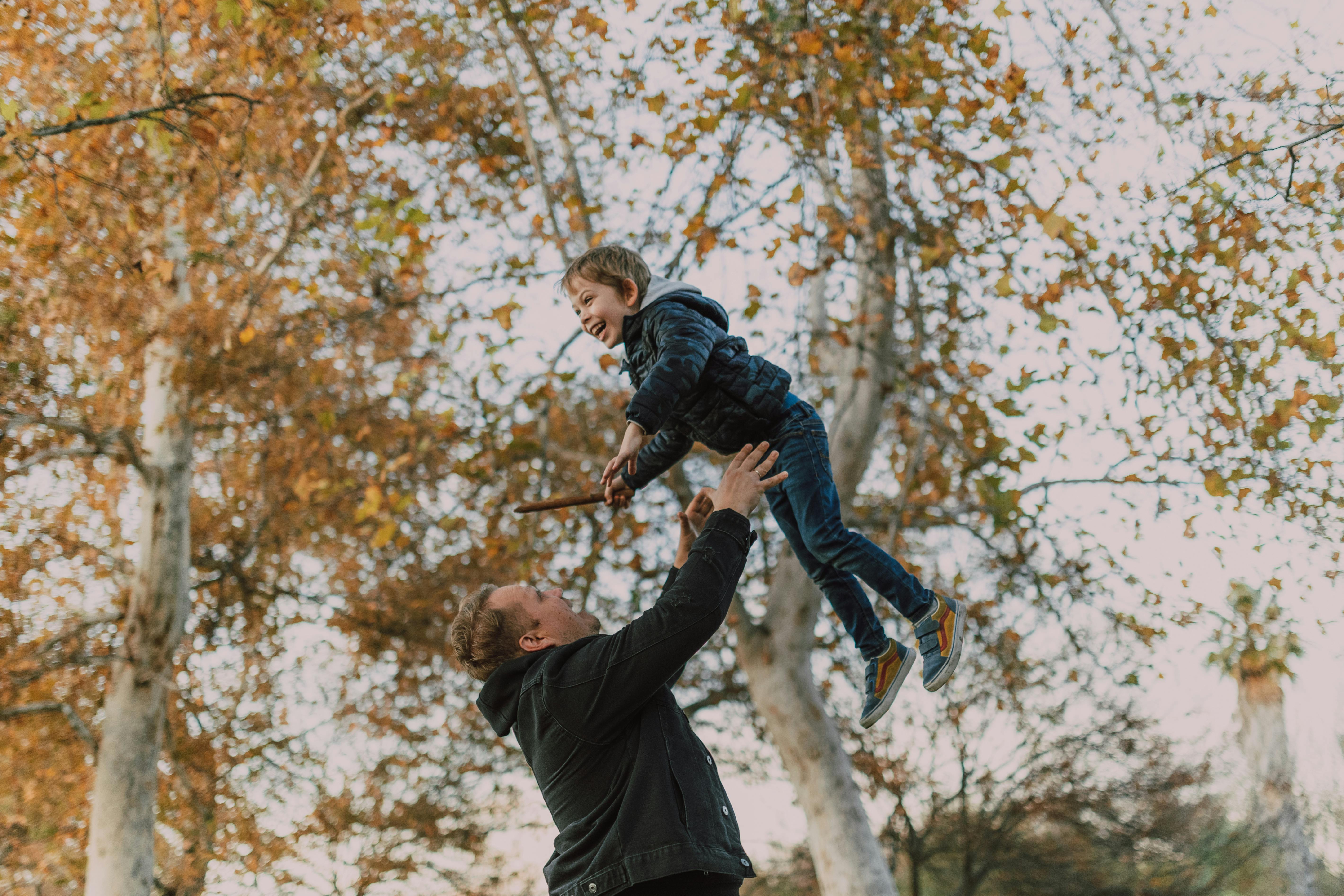 man in black jacket and blue denim jeans jumping on brown tree branch