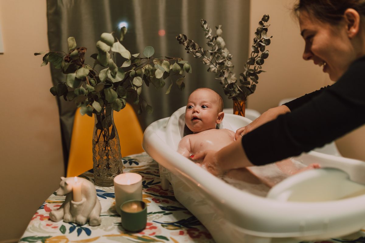 Mother bathing her baby in a small tub surrounded by warm home details