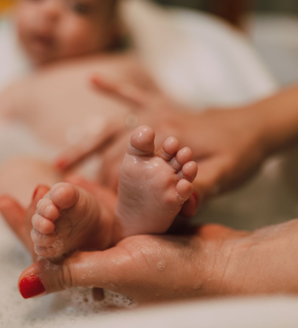 A caregiver gently washing a baby's feet during bath time.