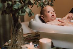 A cute baby in a tub surrounded by candles and greenery on a table indoors.