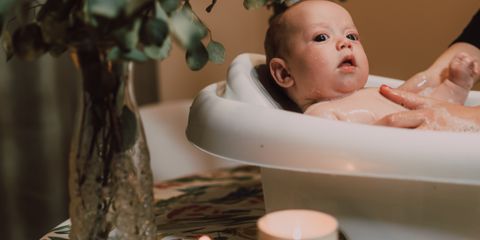 A cute baby in a tub surrounded by candles and greenery on a table indoors.