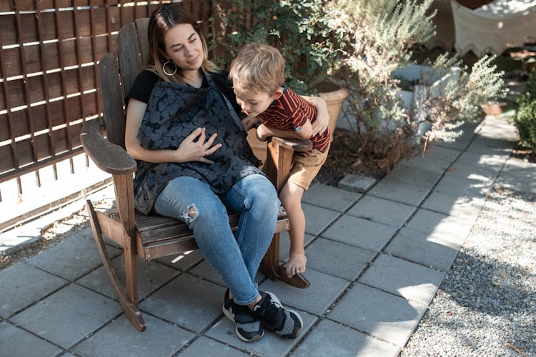 A Pregnant Woman Sitting On A Wooden Armchair Beside Her Son