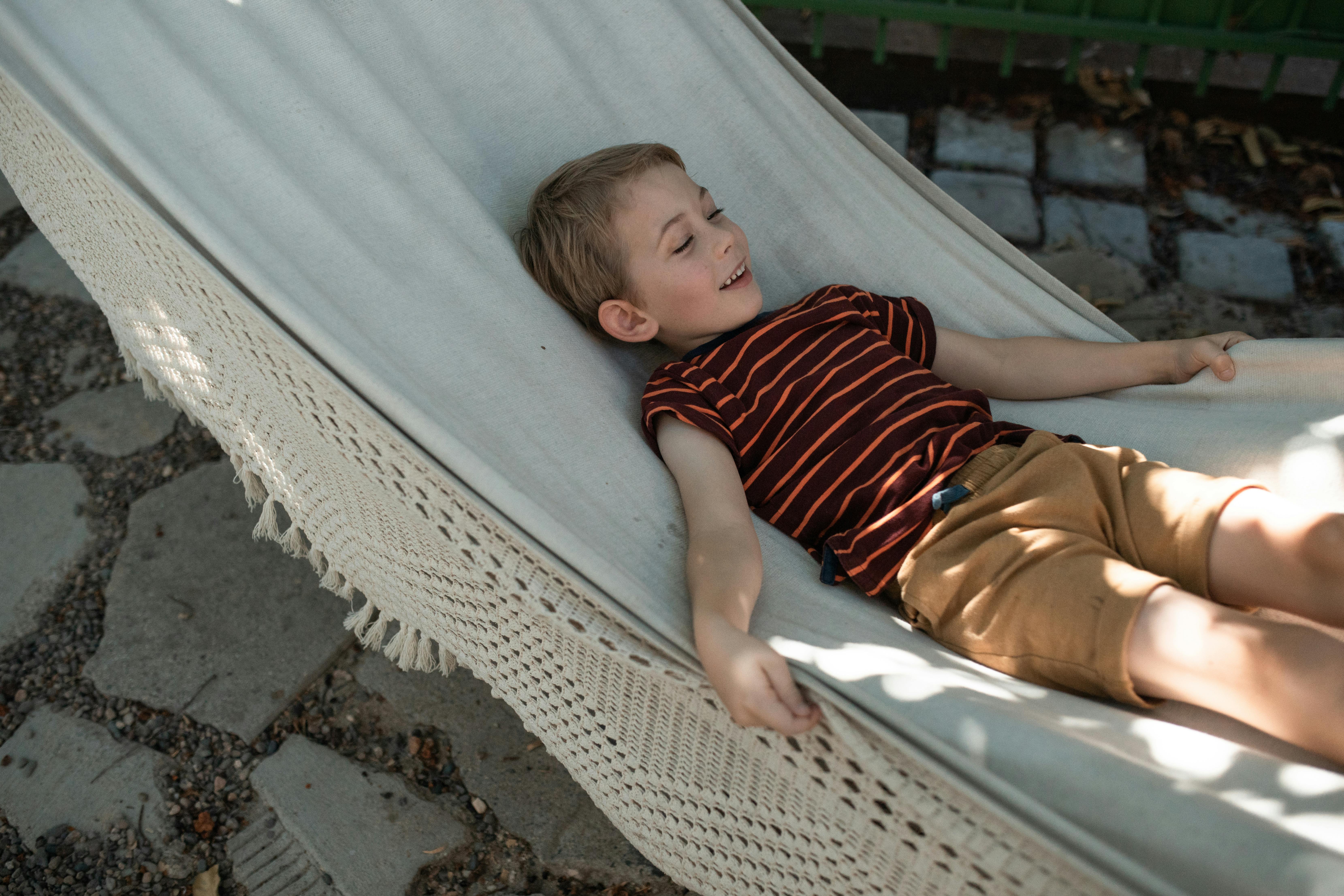 boy in red and white stripe shirt lying on blue and white hammock