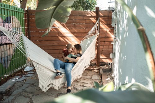 Free Woman Carrying a Baby while Sitting on a Hammock Beside Her Son  Stock Photo