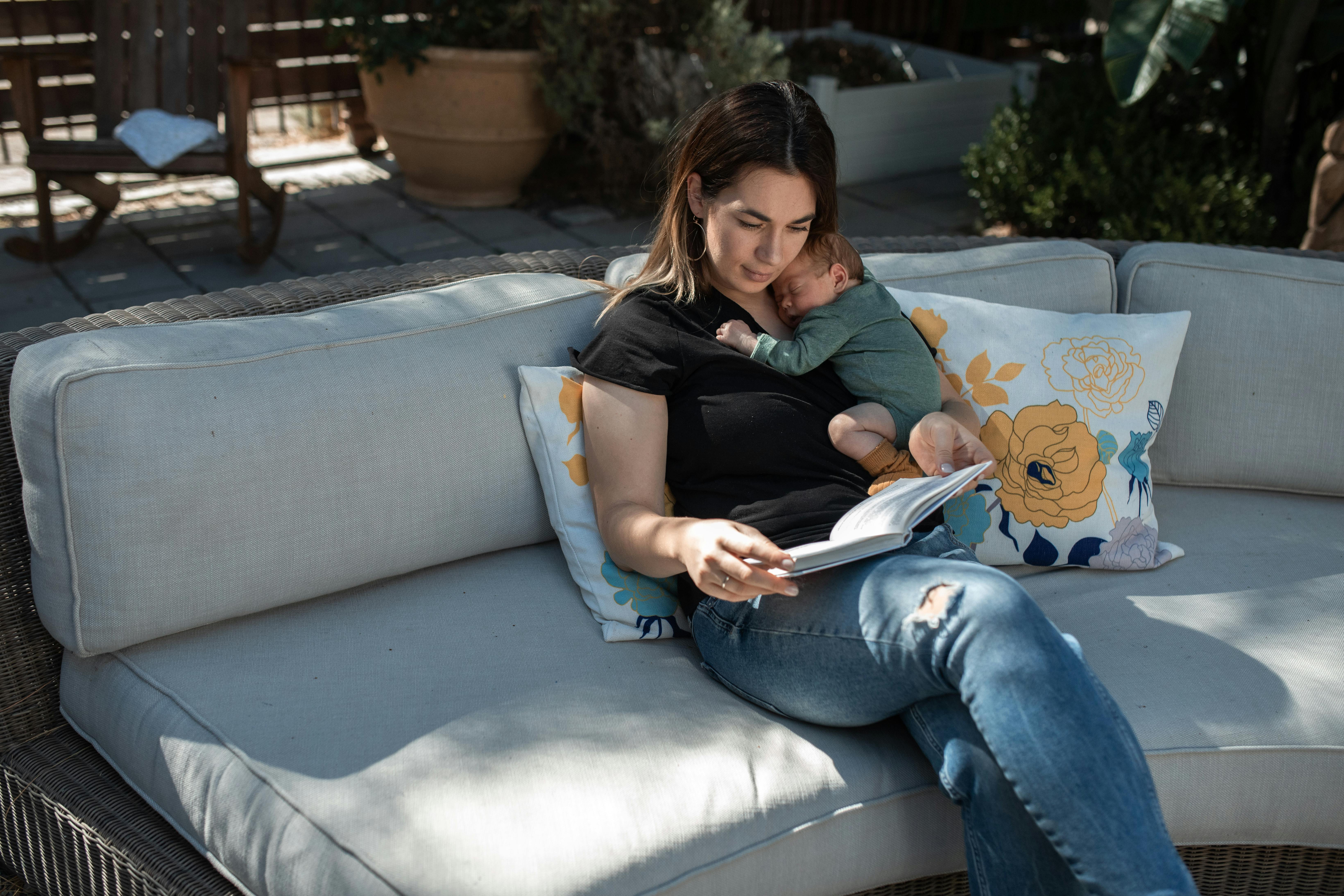 woman in black shirt and blue denim jeans sitting on gray couch reading book