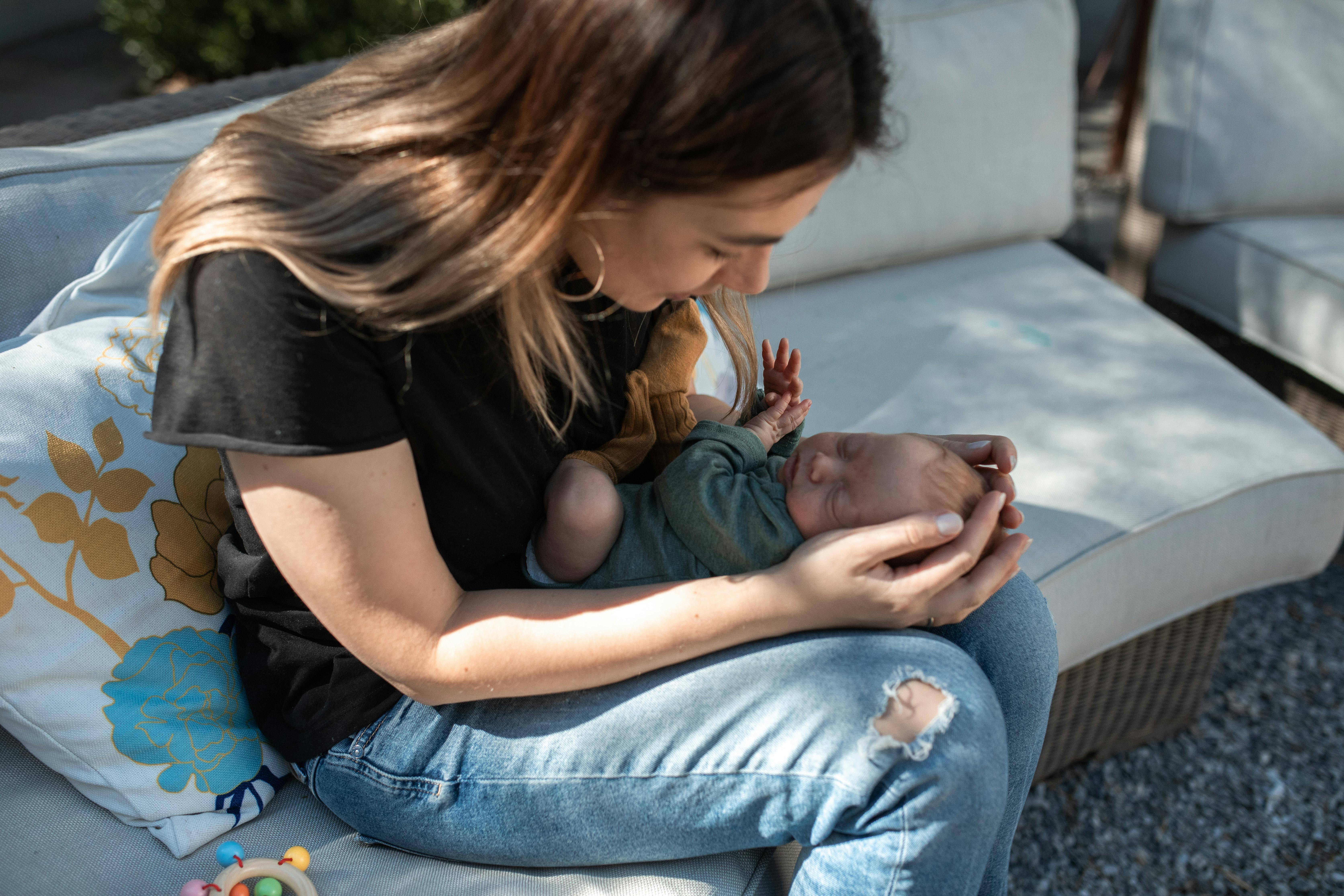 A tender moment captured as a mother cradles her newborn baby on a couch outdoors.