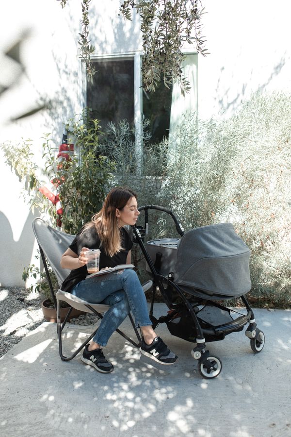 A mother resting outdoors beside a baby stroller