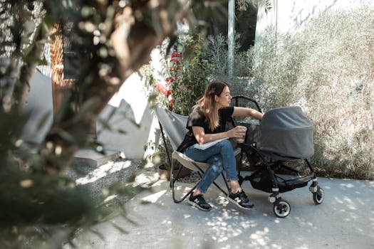 A mother sitting outdoors enjoying a sunny day with her baby in a stroller.