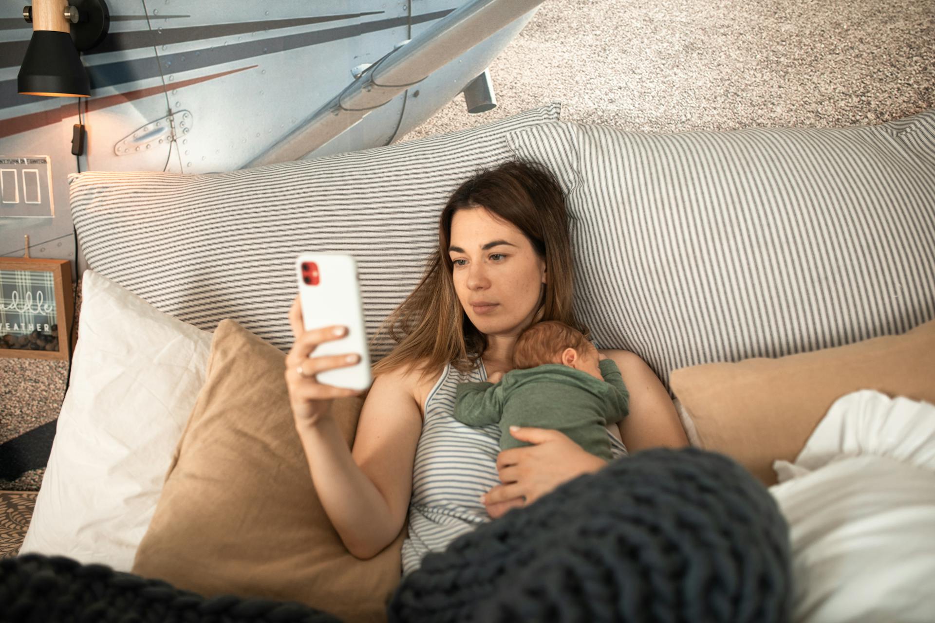 A Woman Lying Down with Her Baby on Her Chest while Using Her Mobile Phone