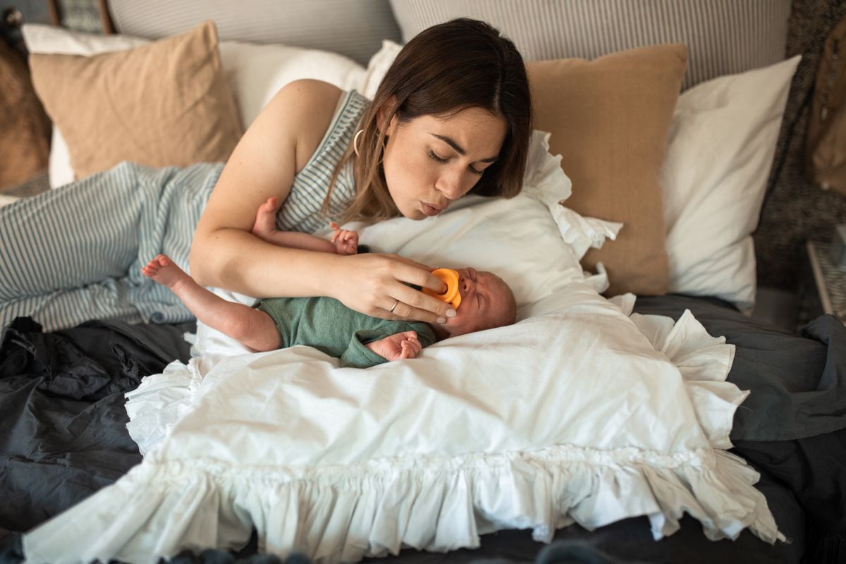 Mother gently soothing her newborn baby while resting on a bed