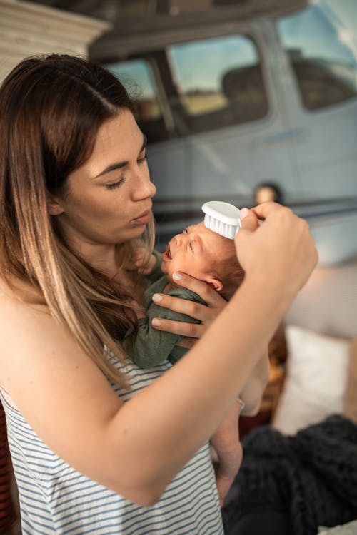 Woman Carrying and Combing Her Baby's Hair