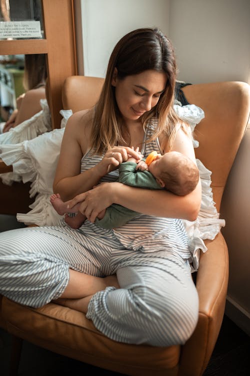 Free A Mother Sitting on a Chair while Carrying Her Baby Stock Photo