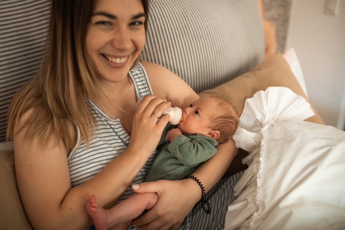 Free A Woman Smiling while Feeding Her Baby with Milk Bottle Stock Photo