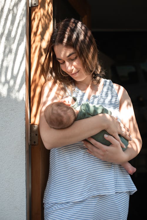 Woman in Blue and White Stripe Shirt Carrying Baby