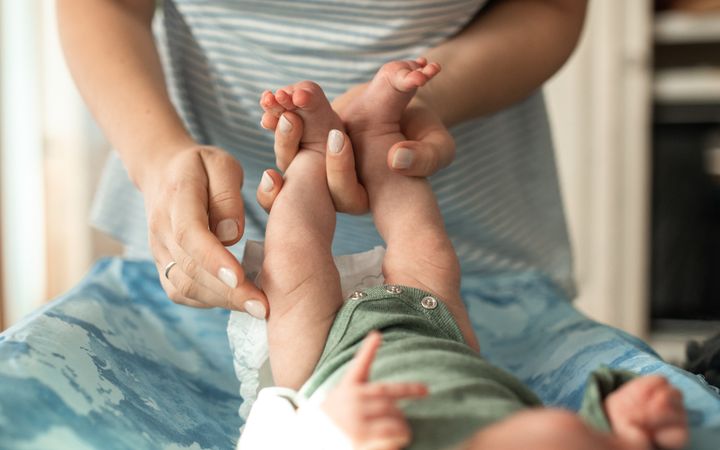 A mother gently changes her baby's diaper indoors with a warm, intimate atmosphere.