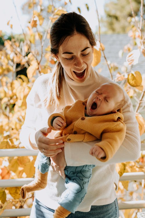 Free Woman in White Sweater Carrying Baby in Brown Sweater Stock Photo