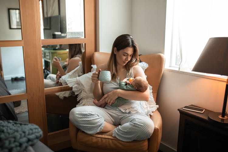 A Woman In A Striped Outfit Carrying Her Baby While Having Coffee