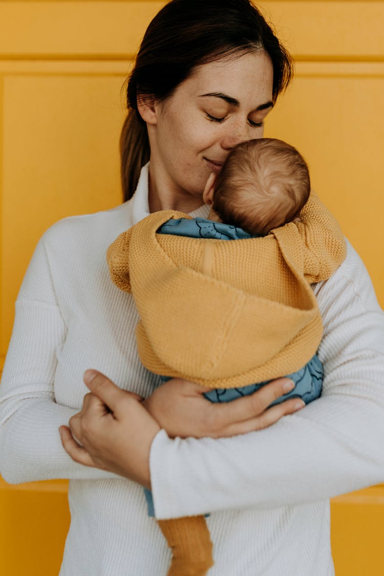 A Woman In White Long Sleeve Shirt Carrying A Baby