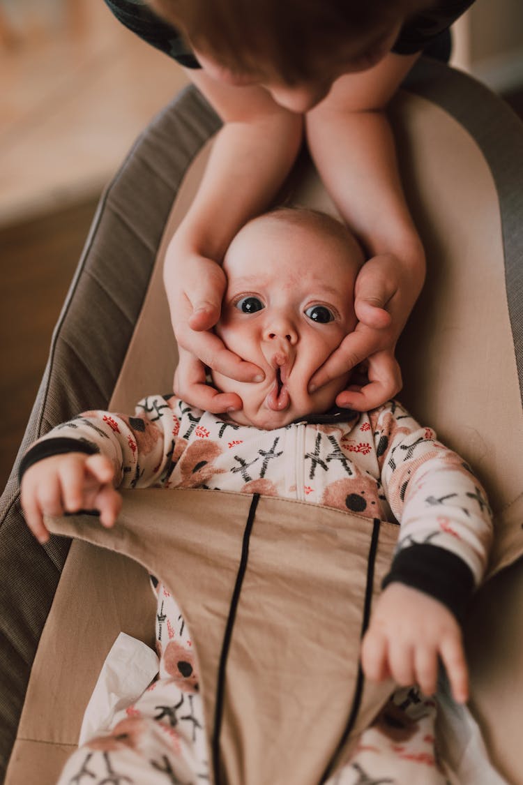 A Kid Squeezing The Face Of A Baby