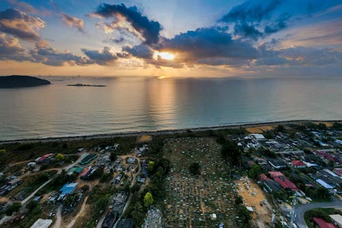 Drone view of small settlement with typical houses located near peaceful sea against picturesque cloudy sunset sky