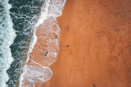Aerial shot of a sandy beach with ocean waves and people enjoying the shoreline.