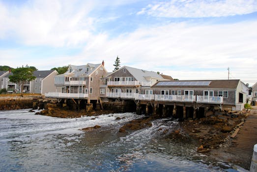 Exteriors of aged residential houses located on rocky coast of wavy ocean against cloudy blue sky