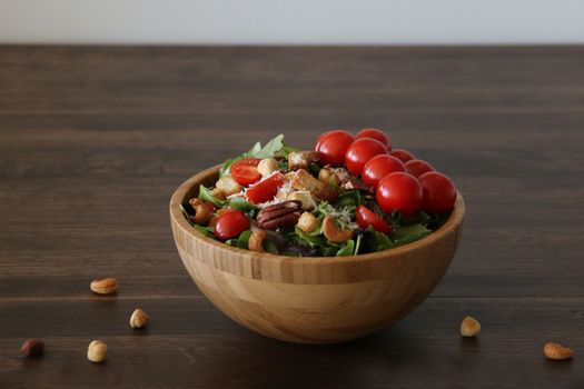 Delicious salad with cherry tomatoes, nuts, and lettuce in a wooden bowl on a rustic table.