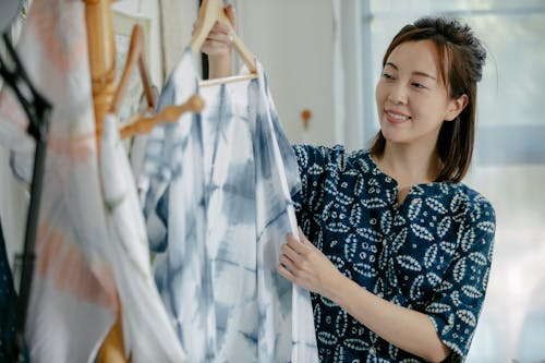 Smiling ethnic woman taking clothes on hanger from rack