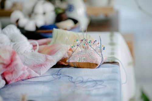 Needles on pillow placed on table with threads and crumpled fabric in sewing studio