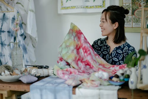 Smiling ethnic seamstress working with colorful fabric in atelier