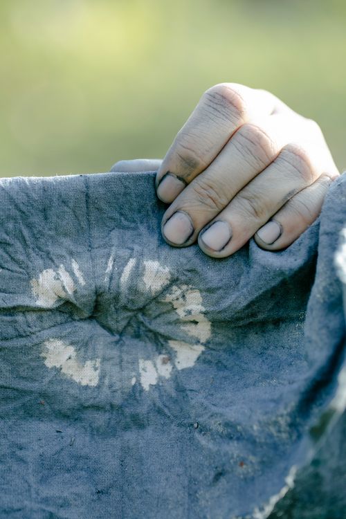 Free Unrecognizable person with painted hands hanging dyed blue fabric with creative round white pattern on sunny street against blurred background Stock Photo