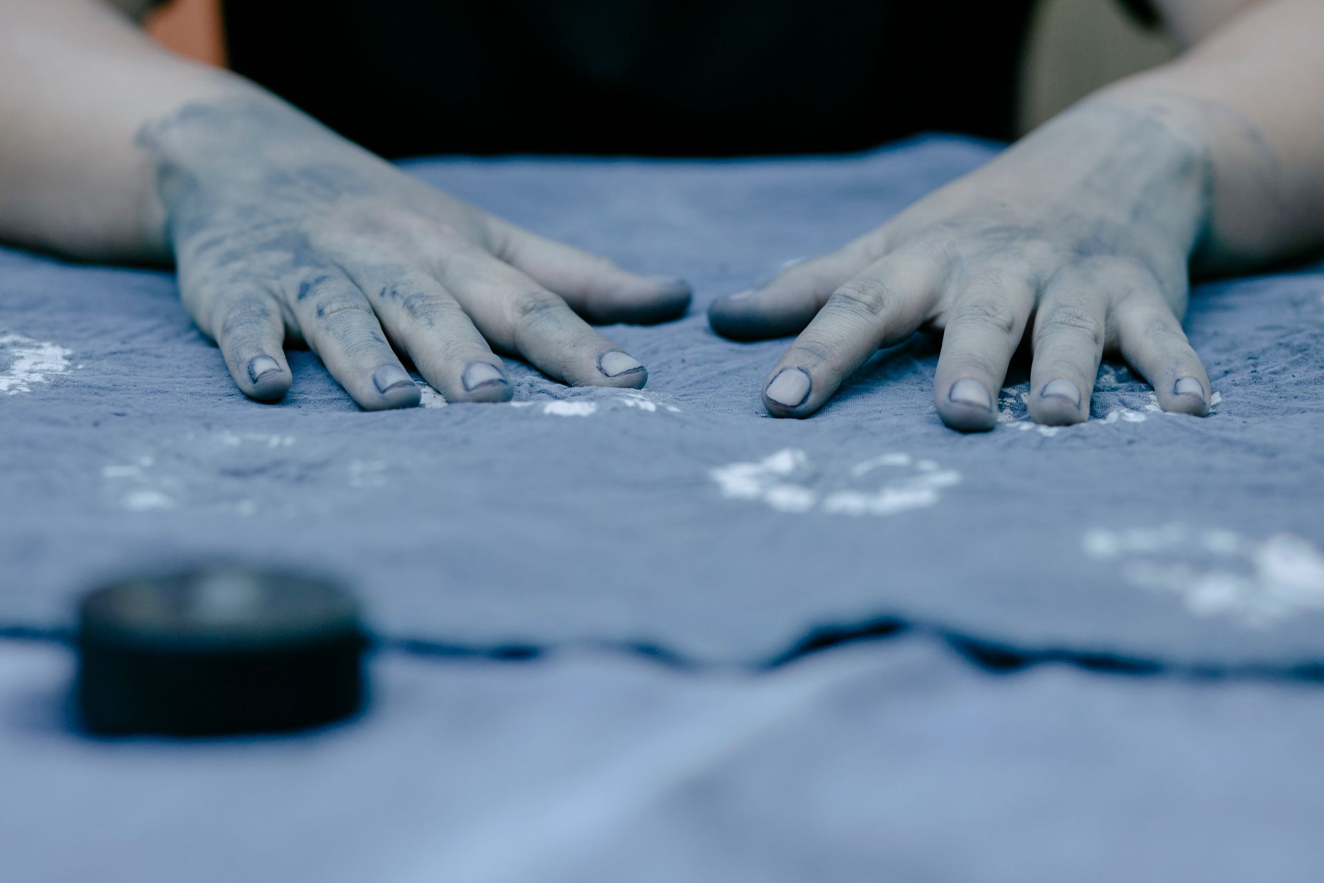 Close-up of hands with blue dye, working on a textile fabric in an artistic workshop setting.