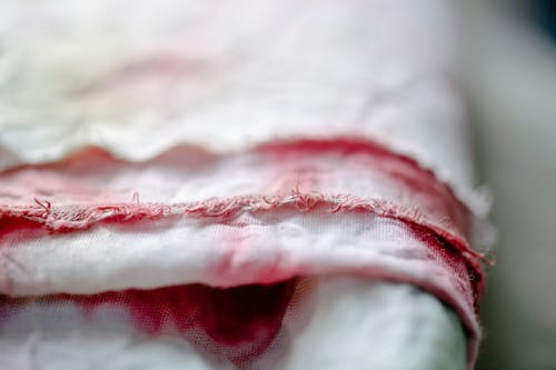 Closeup of rolled creased white textile with dyed pink stains and threads placed on blurred background in light modern studio