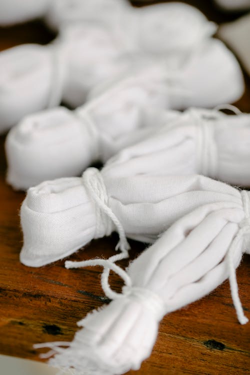 Stack of white fabric tied with ropes placed on wooden surface in light workshop on blurred background while preparing for shibori dyeing