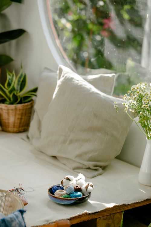 Free From above bowl with various spools of colorful threads and needles placed on wooden platform with soft cushions and plants in sunlight Stock Photo