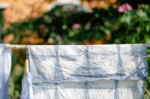Free Crumpled cotton clothes tie dyed in shibori technique handing on bamboo railing in blooming garden on sunny day Stock Photo