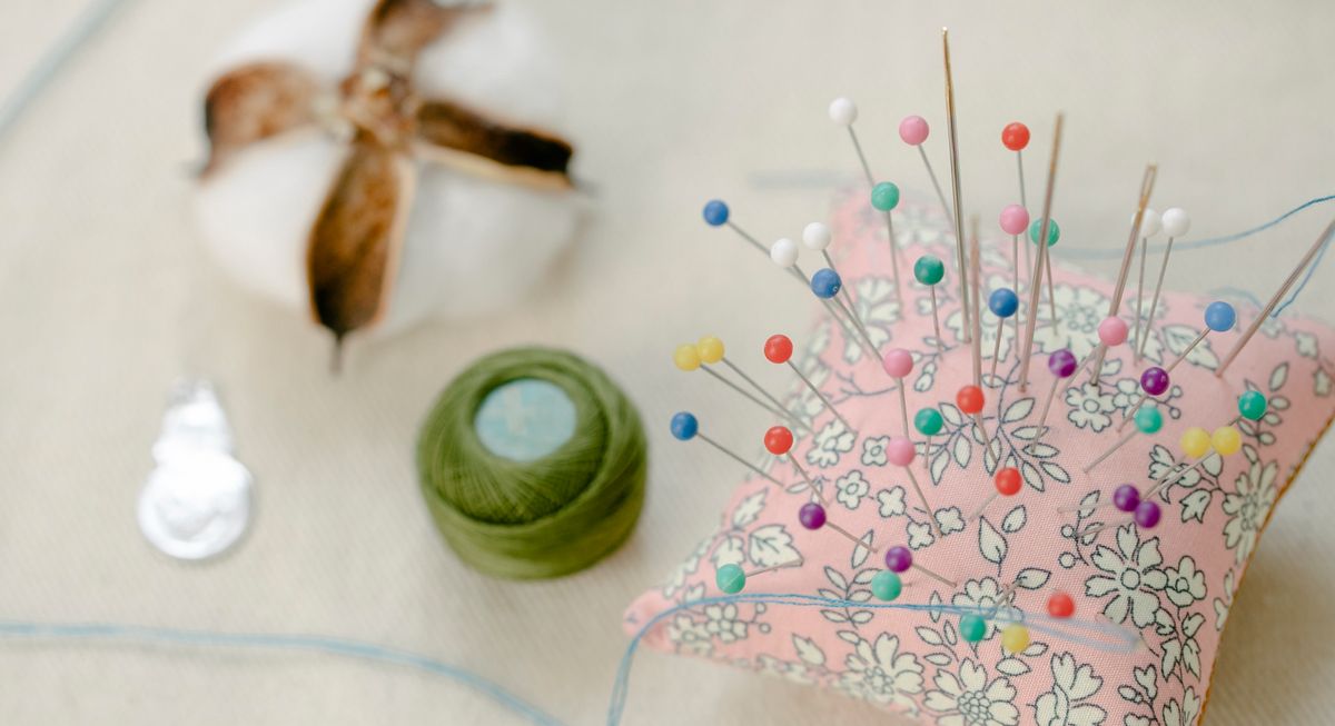 Colorful sewing pins on a small pillow with a thread roll nearby