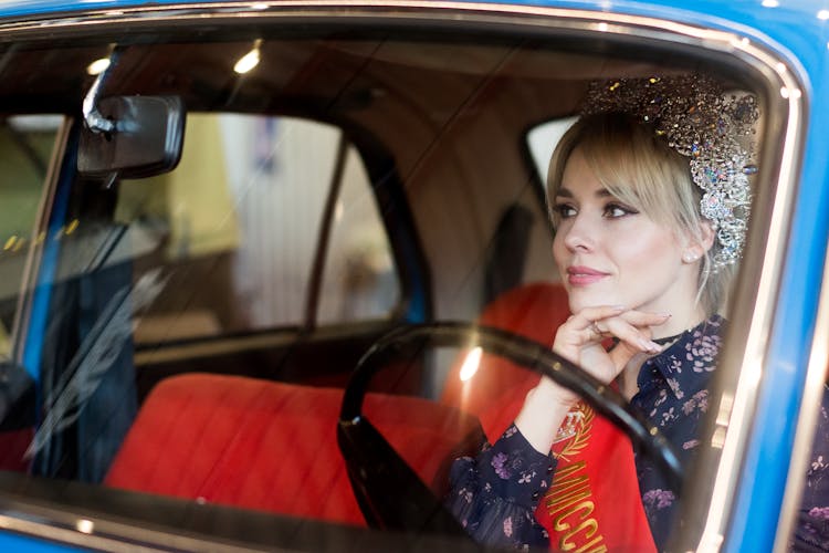 Confident Lady In Crown With Ribbon Sitting In Vintage Vehicle