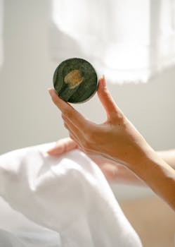 Crop anonymous female holding white fabric and natural soap against blurred light background